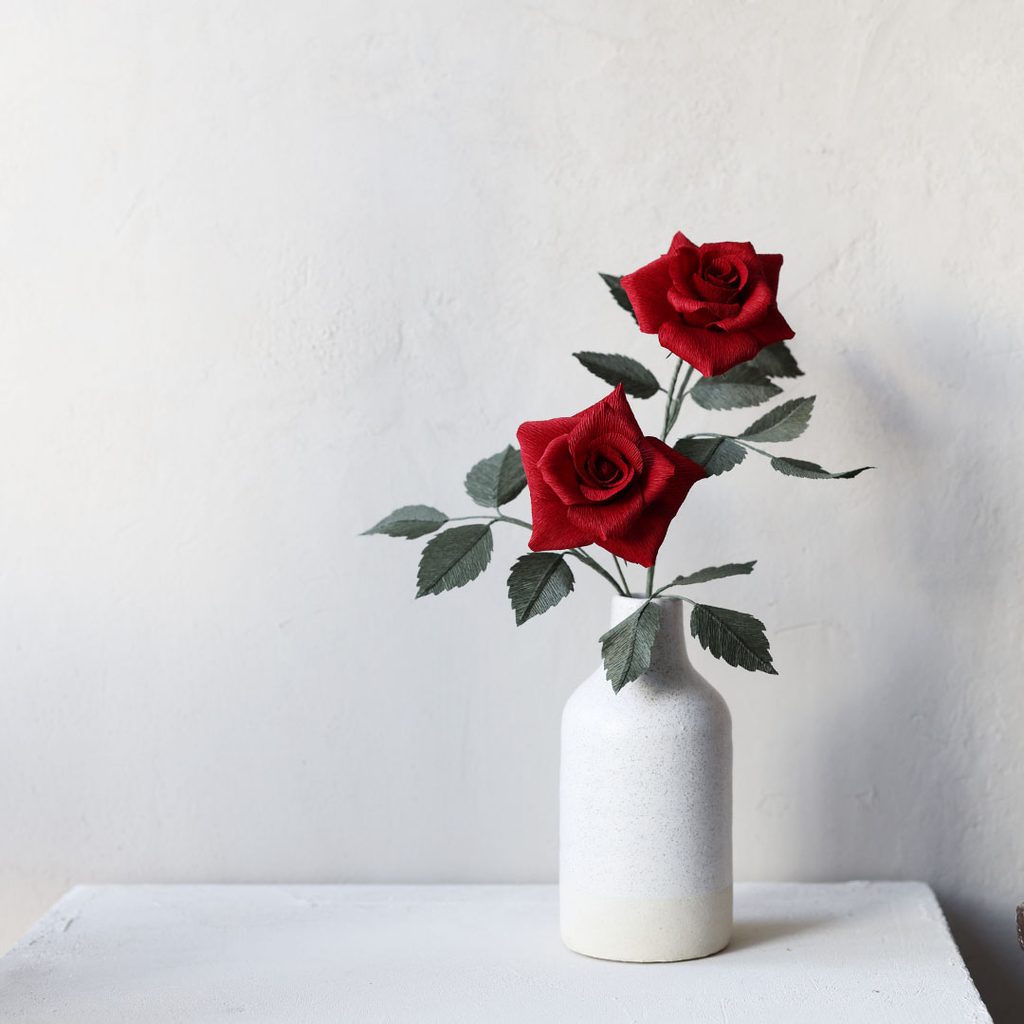 Red crepe paper roses in a white vase