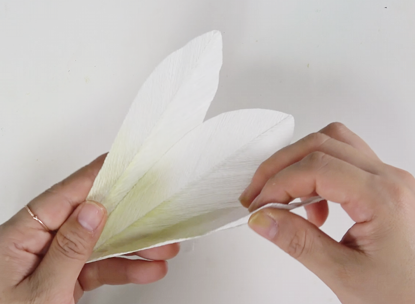 Attaching dark green crepe paper leaves along the stem of a finished paper lily