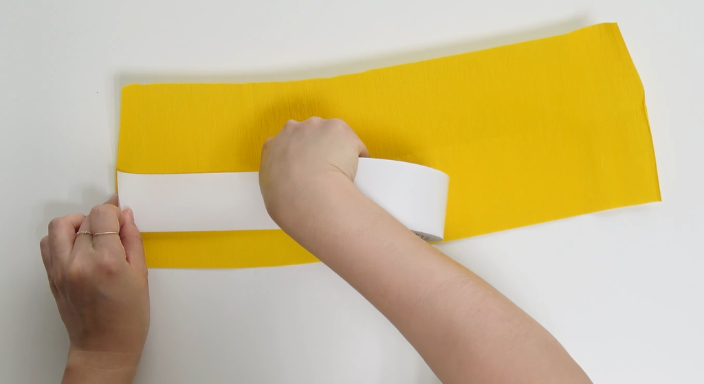 Applying double-sided tape to yellow crepe paper for a giant daisy center