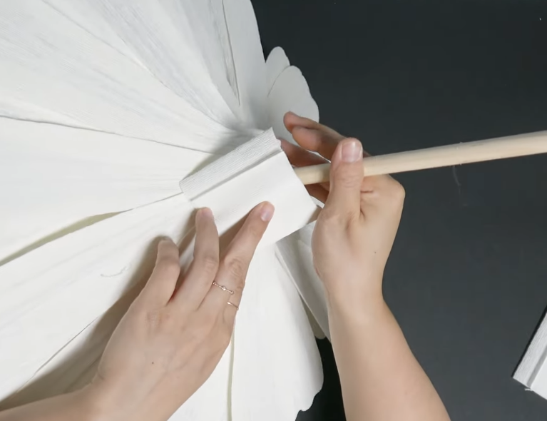 Wrapping white crepe paper around the back of a giant daisy flower to finish the base
