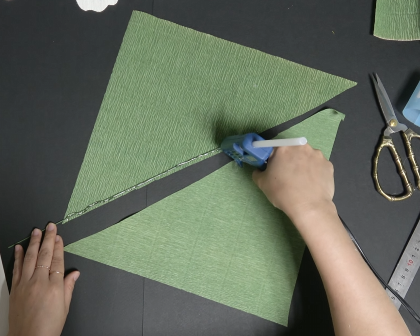 Gluing floral wire between green crepe paper layers to make a giant daisy leaf