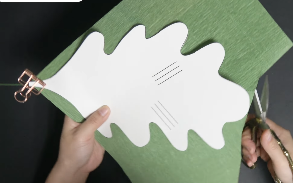 Cutting green crepe paper with a leaf template for a giant daisy