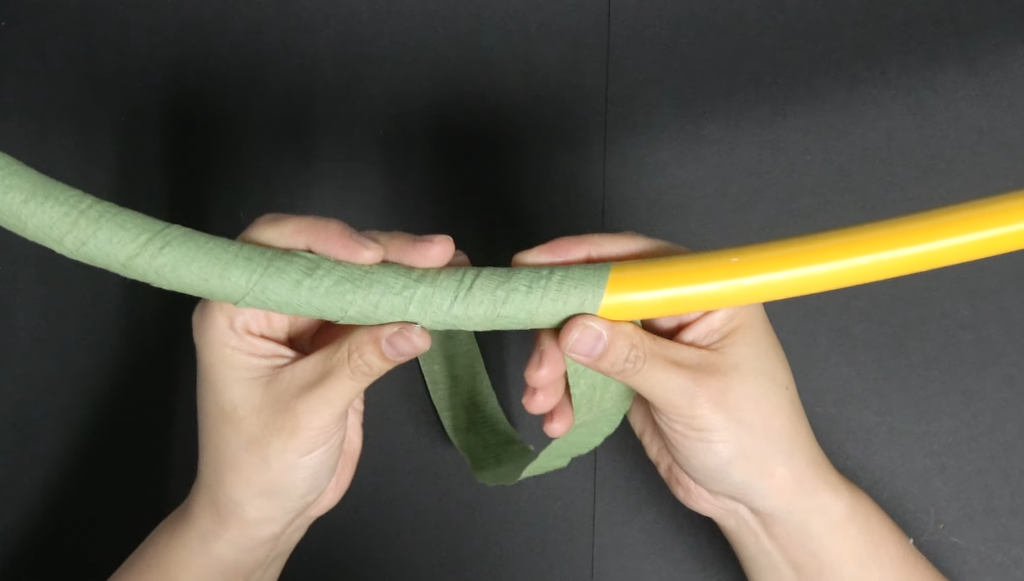 Wrapping green crepe paper around a flexible pipe to make a giant daisy stem