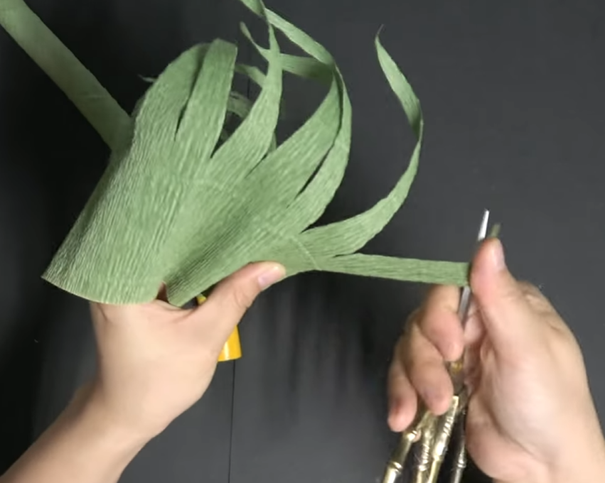 Curling pointed green crepe paper strips with scissors to make grass for a giant daisy