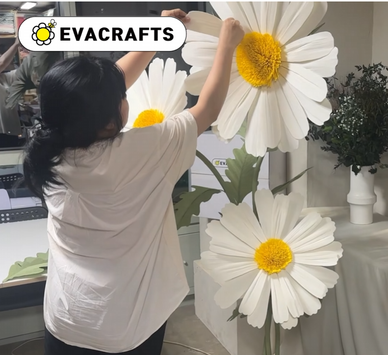 Woman assembling three finished giant white paper daisy flowers with yellow centers