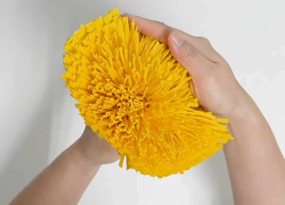 Fluffing the yellow crepe paper fringe to shape the center of a giant daisy