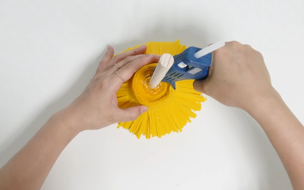 Securing the giant daisy center with hot glue around a wooden stick