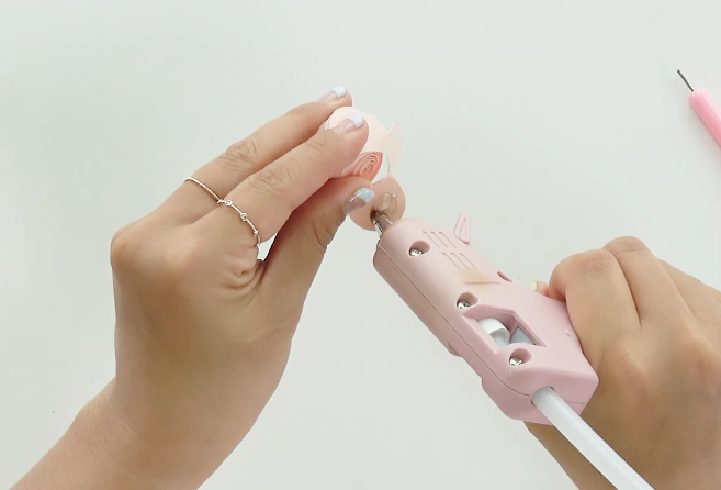 Applying hot glue to the rolled center of a pink paper flower during a DIY paper flower bouquet tutorial.