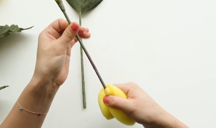 Applying purple oil pastel to the lower stem of a handmade paper calla lily