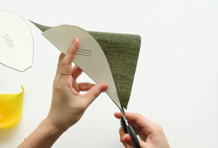 Cutting dark green crepe paper with a leaf pattern for the calla lily