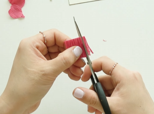 Cutting thin fringes into pink crepe paper to make flower stamens