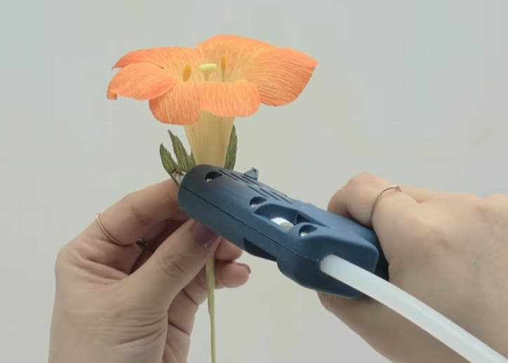 Attaching green crepe paper calyx pieces to the base of a trumpet vine flower