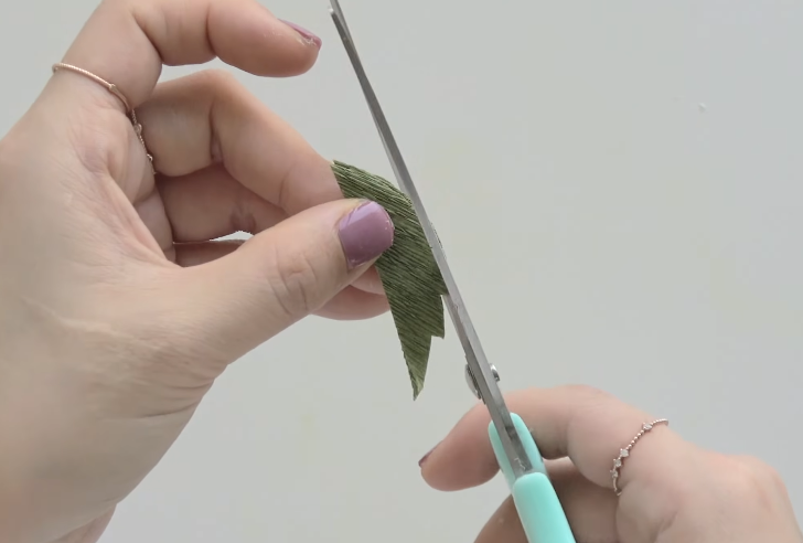 Cutting serrated edges into green crepe paper trumpet vine leaves