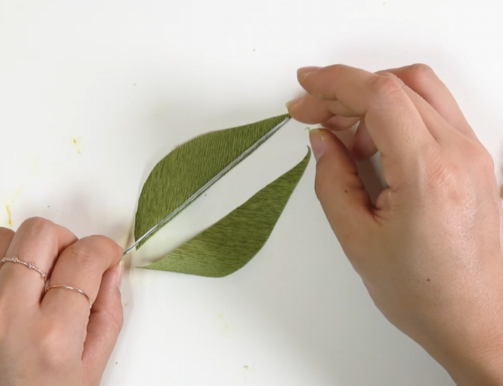 Attaching floral wire between two green crepe paper leaf pieces
