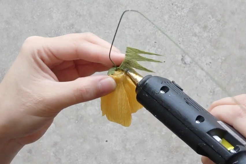 Gluing a green crepe paper calyx underneath the handmade cosmos flower