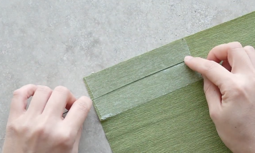 Placing green wire between crepe paper layers with double-sided tape to make cosmos leaves