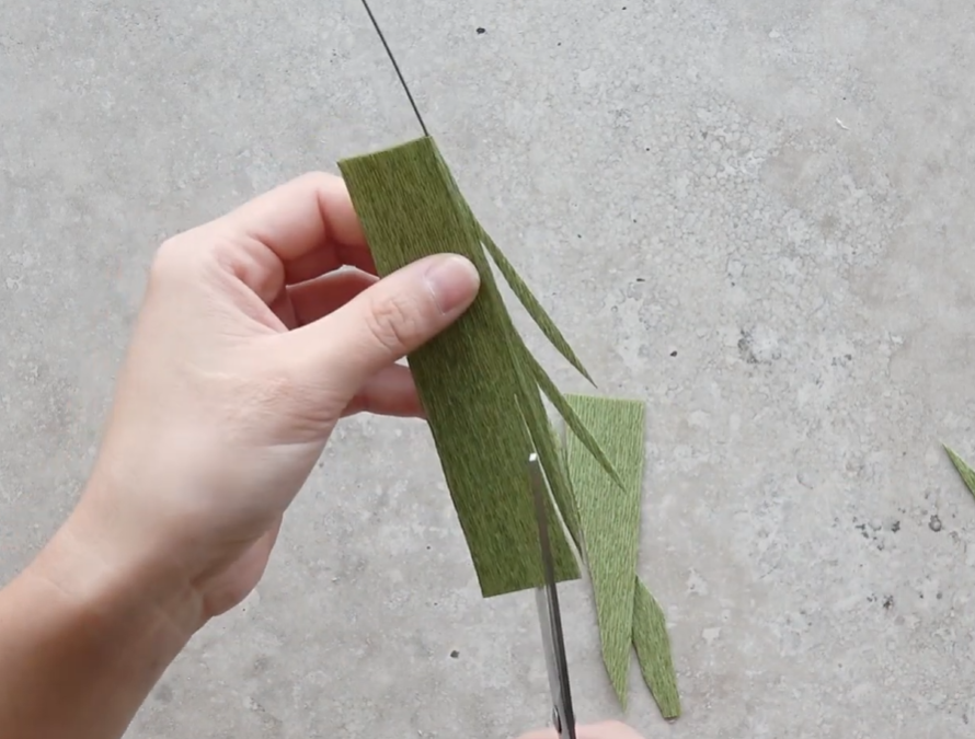 Cutting narrow pointed cosmos leaves from green crepe paper around the center wire