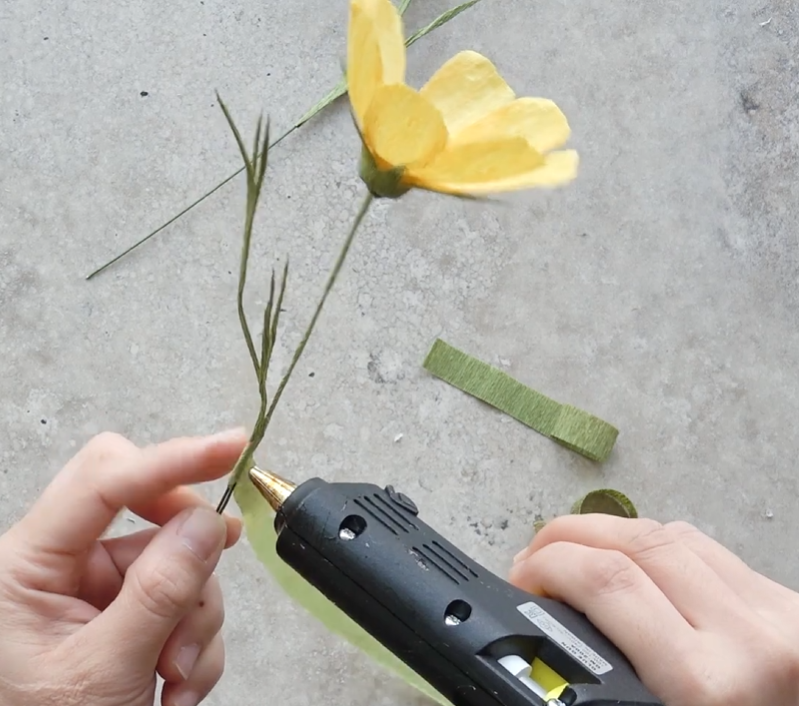 Attaching handmade crepe paper leaves along the cosmos flower stem with hot glue