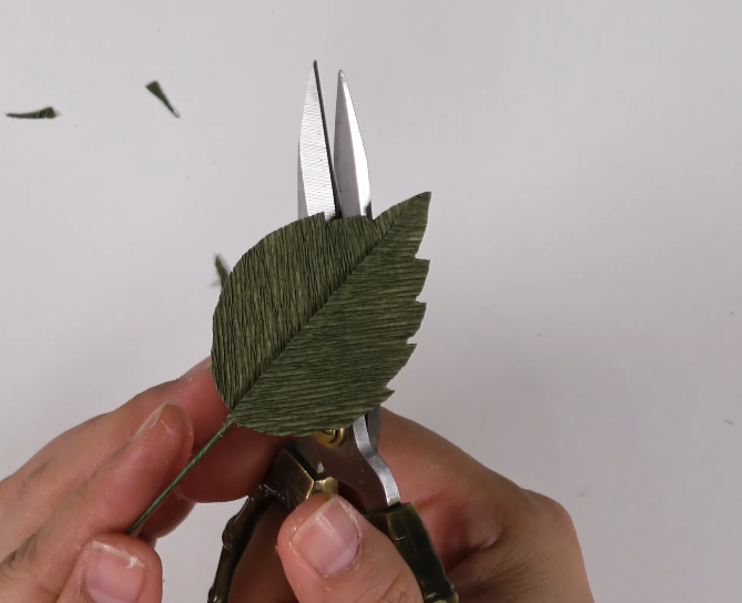 Cutting the edges of a green crepe paper rose leaf into a serrated shape