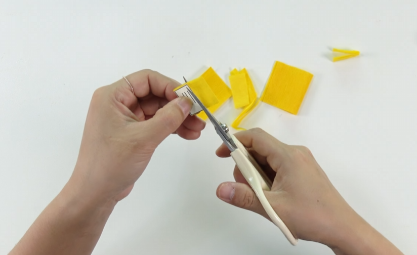 Cutting yellow crepe paper pieces to make the center of a handmade crepe paper zinnia flower.
