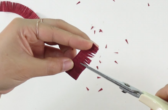 Trimming burgundy crepe paper fringes into pointed tips for the center of a handmade crepe paper zinnia.