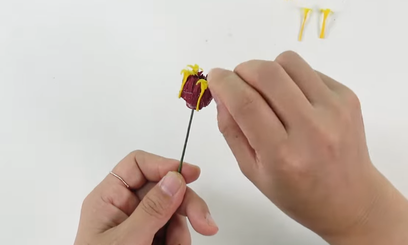 Attaching small yellow crepe paper stamens around the burgundy center of a handmade crepe paper zinnia.