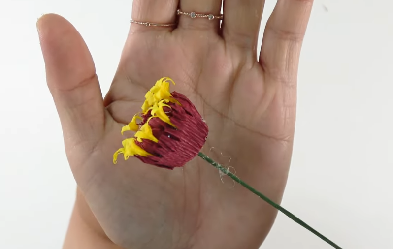 Completed burgundy and yellow crepe paper zinnia flower center attached to green floral wire.