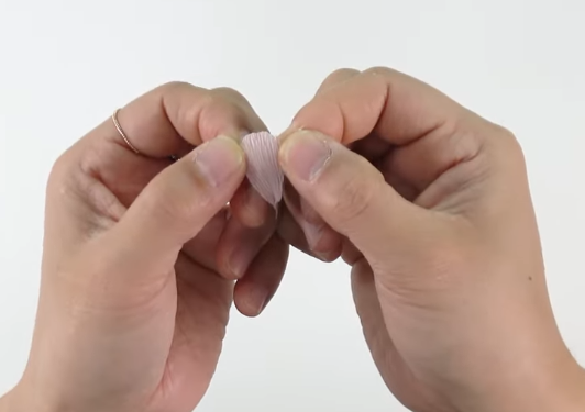 Shaping a light pink crepe paper zinnia petal by gently stretching the center with both hands