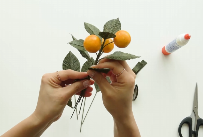 Inserting green floral wire into a finished kumquat fruit for the citrus garland