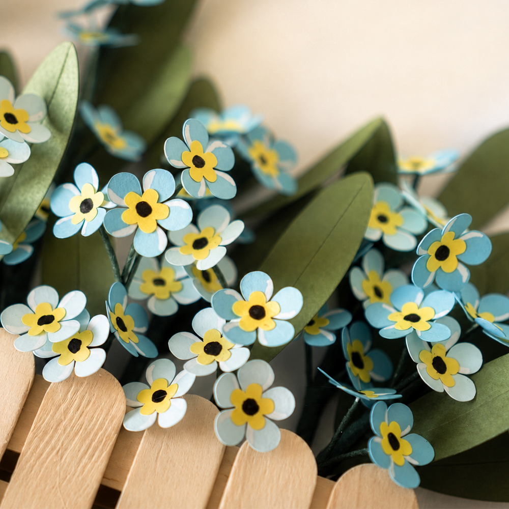 Close-up of handmade forget-me-not paper flowers with blue petals and green leaves for paper flower wall art