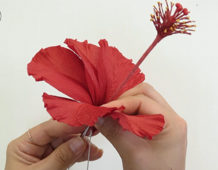 Attaching five large red petals around the stamen of a realistic crepe paper hibiscus