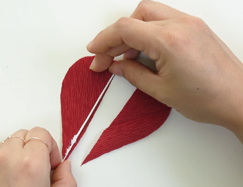 Gluing white floral wire between two red crepe paper petal layers in a V-shaped grain direction