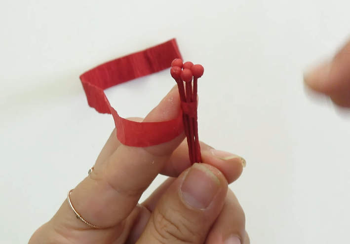 Joining five handmade hibiscus pistil pieces together with red crepe paper