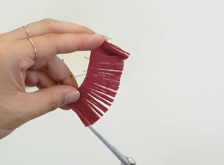 Cutting burgundy crepe paper into fine fringes to make hibiscus stamens
