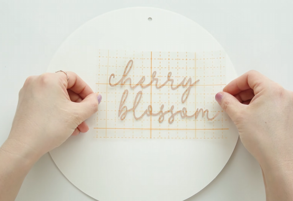 Applying rose gold cherry blossom lettering to the round paper board with transfer tape