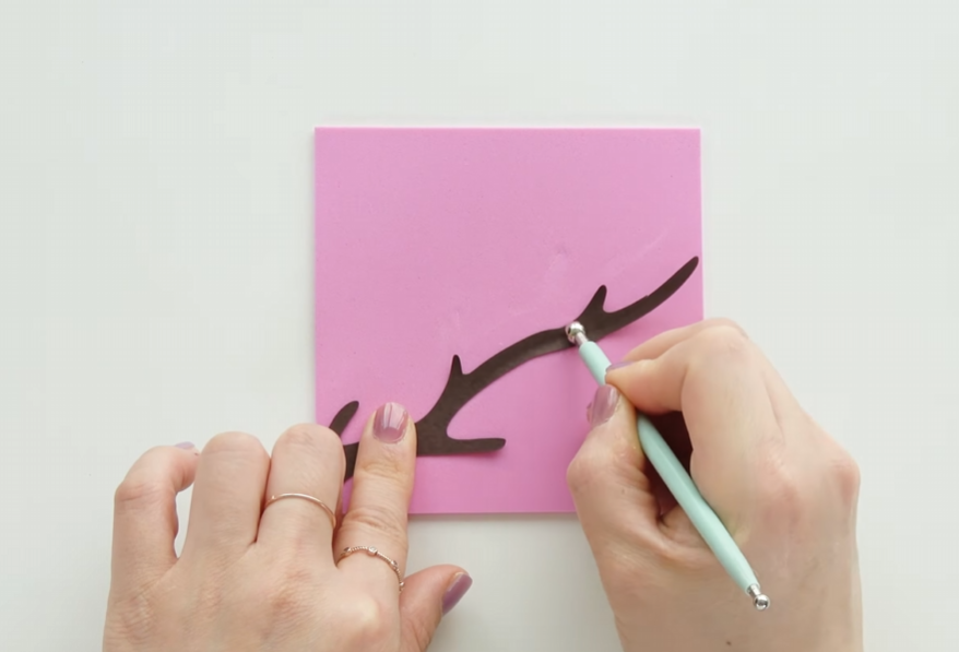 Shaping a brown cardstock branch with a ball tool on an EVA foam sheet