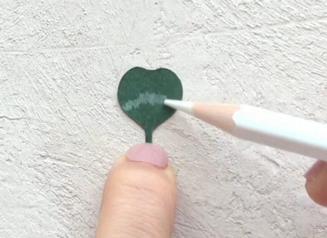 Drawing a white pencil pattern on a green paper shamrock leaf