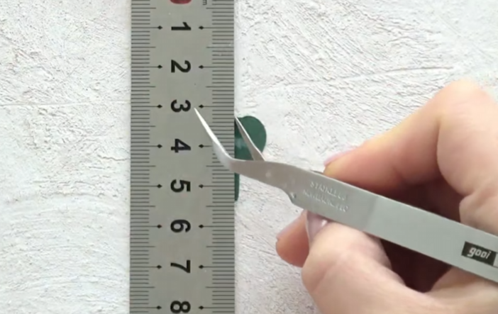Measuring a green paper shamrock leaf with a ruler and tweezers