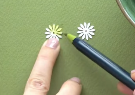 Coloring the center of small white paper flowers with a light green brush pen