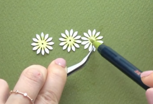 Coloring the center of a white paper flower with a light green brush pen while holding it with tweezers