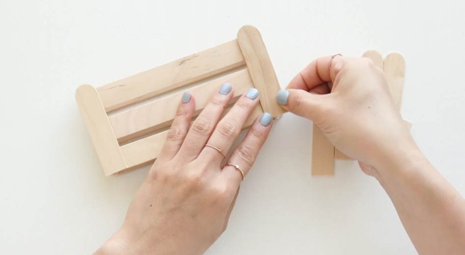 Assembling wooden craft sticks into a small fence for paper flower wall art