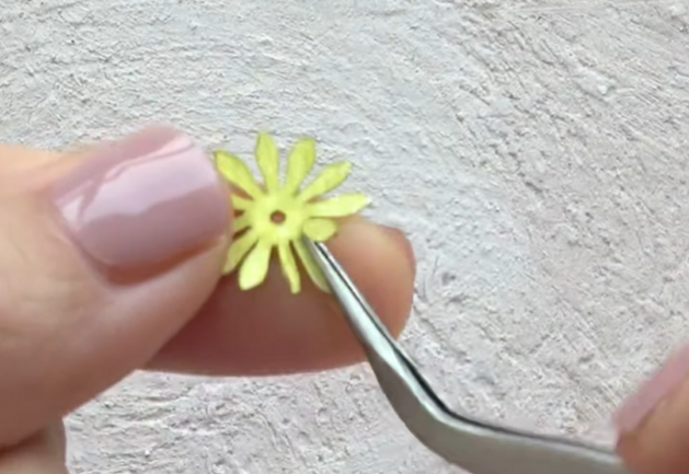 Shaping the petals of a small paper flower with tweezers