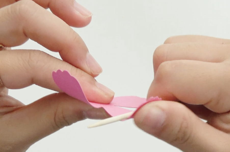 Shaping pink cardstock petals with a thin wooden stick while making a cosmos paper flower.
