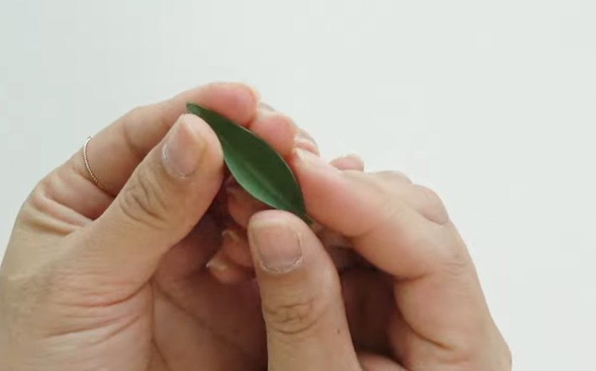 Shaping a green paper leaf by folding it gently along the center for a dogwood paper flower wreath