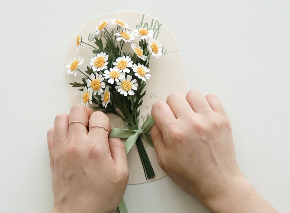 Tying the finished mini daisy paper flower bouquet onto a message card with ribbon