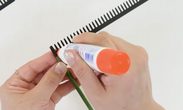 Applying glue to a black cardstock center strip before wrapping it around the sunflower stem