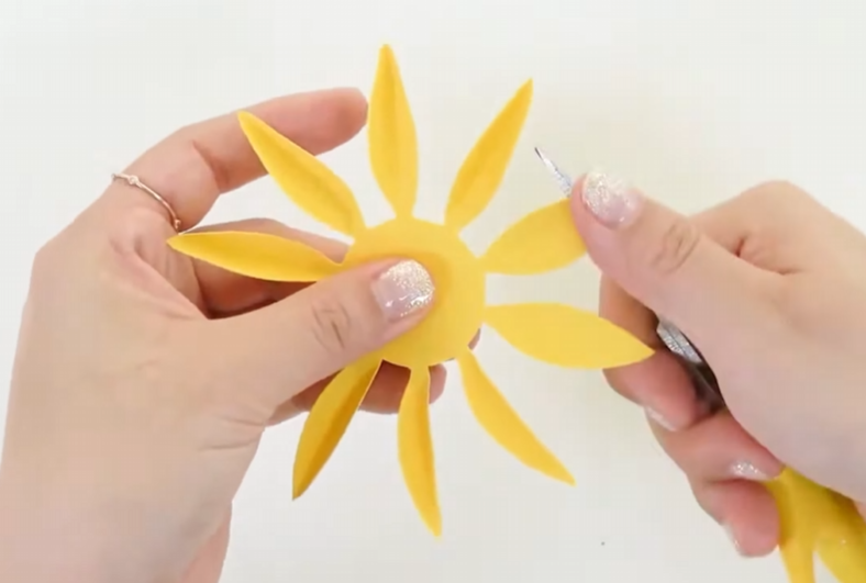 Curling the tips of yellow cardstock sunflower petals with scissors
