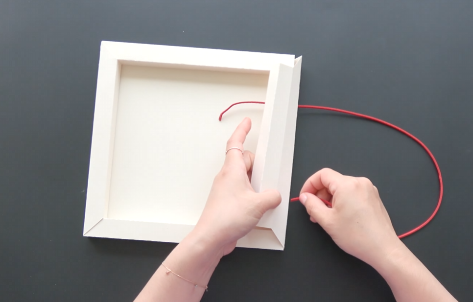 Attaching red ribbon to the top of the handmade white paper frame