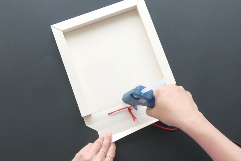 Securing the top of the paper frame with hot glue and red hanging ribbon