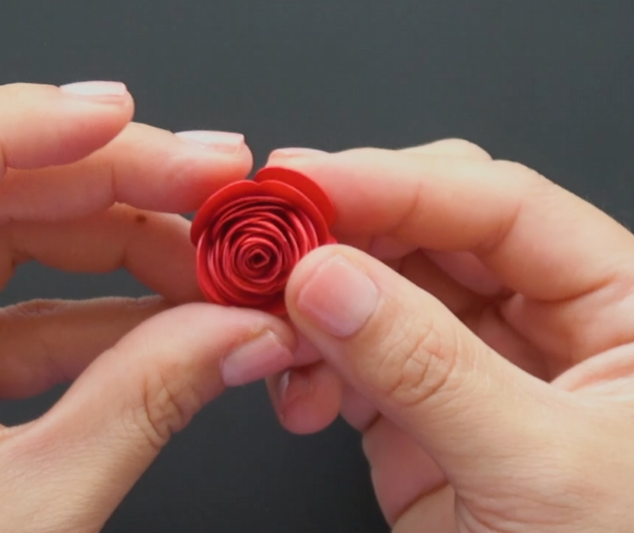 Loosening a rolled red paper rose to create a fuller flower shape